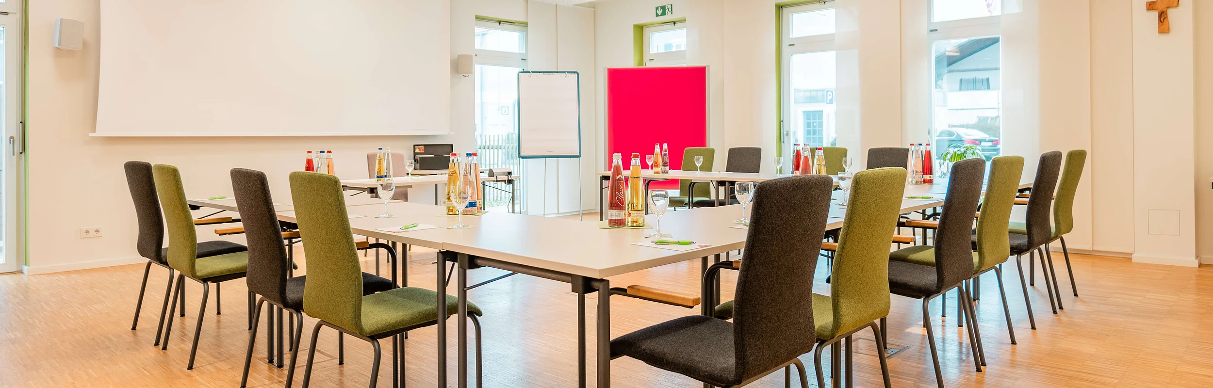 In einem Raum mit einer U-Form Tische und Stühle stehen Getränke und ein Beamer mit Leinwand bereit für Tagungen im Hotel die Krone Kinding.