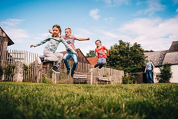 Drei Kinder springen über ein Seil im Garten, zwei weitere halten das Seil gespannt.