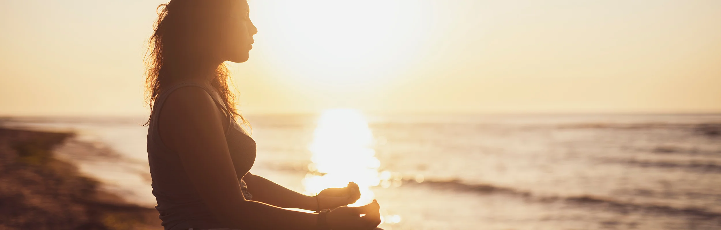 Sonnenuntergang am Meer. Eine Frau sitzt meditierend am Meerufer