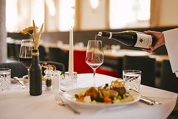 Wein wird in ein Glas auf einem gedeckten Tisch mit Kerze und Essen in einem Restaurant eingeschenkt.