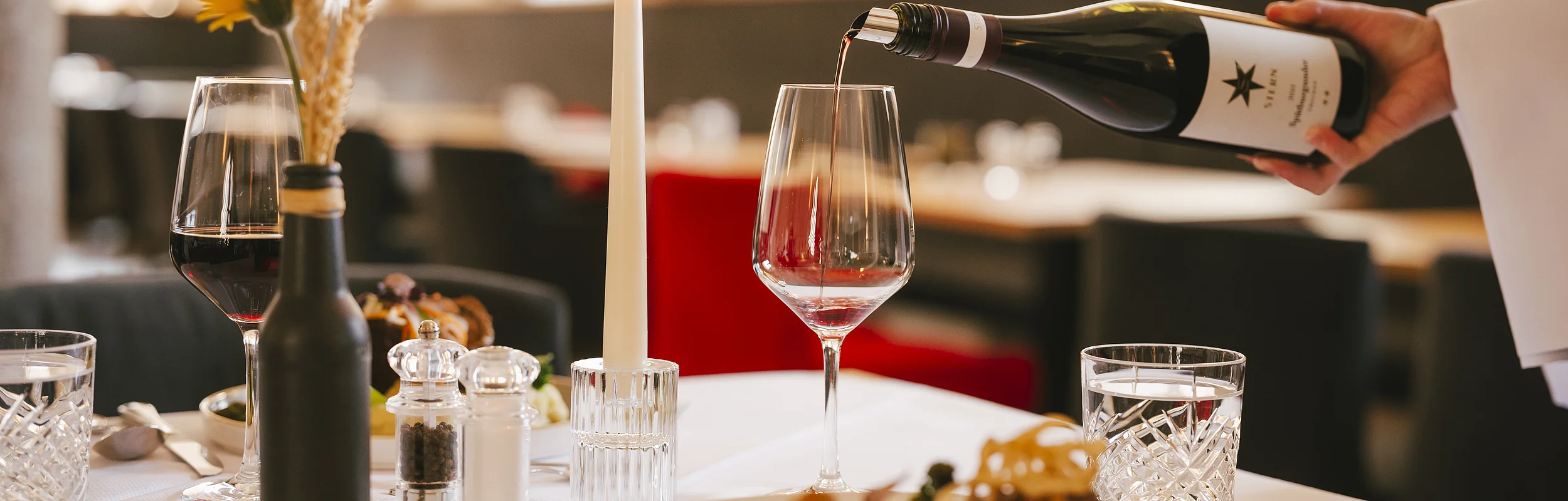 Wein wird in ein Glas auf einem gedeckten Tisch mit Kerze und Essen in einem Restaurant eingeschenkt.