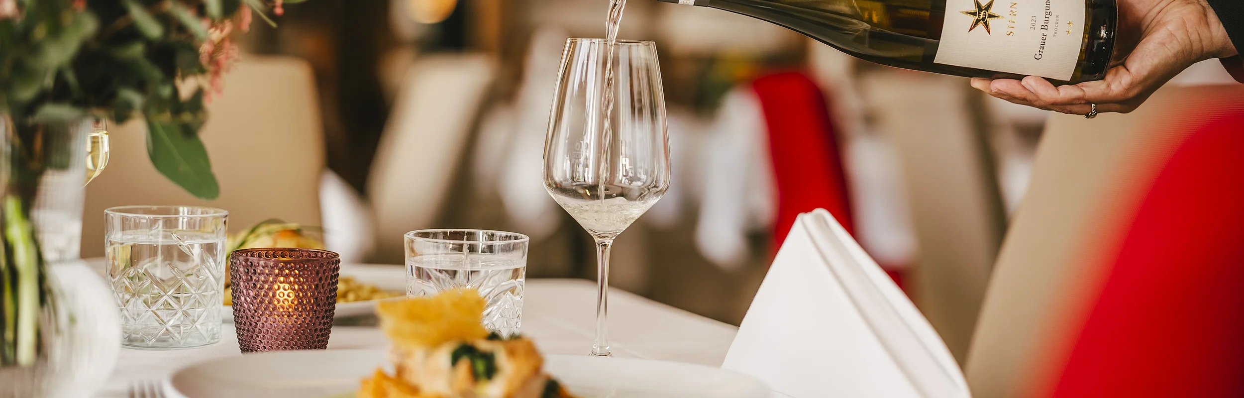 Wein wird aus einer Flasche in ein Weinglas auf einem gedeckten Tisch in einem Restaurant eingeschenkt.