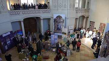Innenraum mit Ständen und Menschen auf einer Messe oder Ausstellung in einem historischen Gebäude