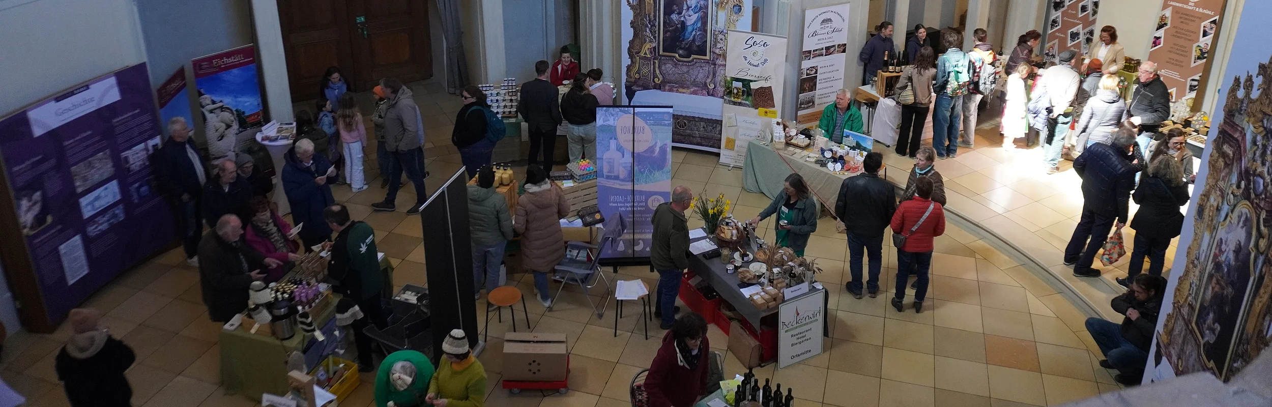 Innenraum mit Ständen und Menschen auf einer Messe oder Ausstellung in einem historischen Gebäude