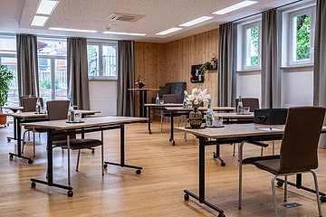 Konferenzraum mit mehreren Tischen und Stühlen, Wasserflaschen, Gläsern und Blumen auf den Tischen.