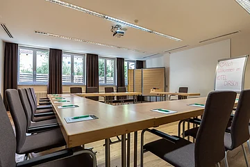 Konferenzraum mit U-förmigen Tischen, Stühlen, Flipchart und Tageslichtfenstern im Hotel Dirsch.