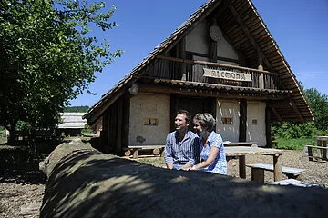 Ein Paar sitzt vor dem Keltenhaus im Erlebnisdorf Alcmona.